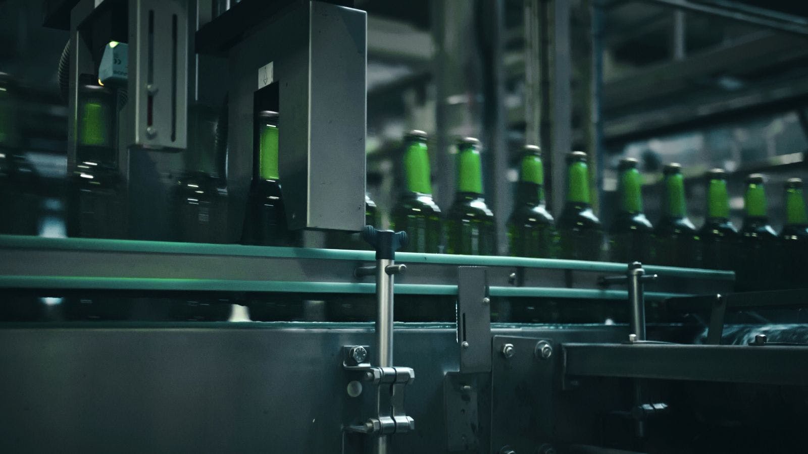 Rows of green glass bottles gliding along a conveyor belt inside an industrial brewery, moving through quality control machinery designed for efficient production and inspection